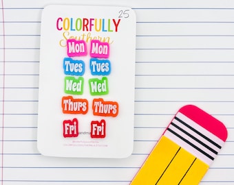 May include: A set of ten colorful day-of-the-week stickers arranged in two columns on a white backing card. The stickers feature the text Mon, Tues, Wed, Thurs, and Fri in bright pink, blue, green, orange, and red. A pencil-shaped cutout is nearby.