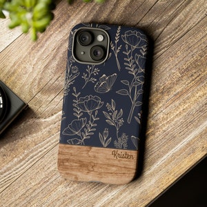 May include: A navy blue phone case with a wood accent and a floral design in gold. The case has the name "Kristen" engraved on the wood accent.