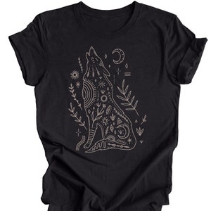 Puede incluir: Camiseta negra con un dibujo lineal de un lobo aullando con una luna creciente y otros s&iacute;mbolos celestiales. El lobo est&aacute; rodeado de plantas estilizadas.
