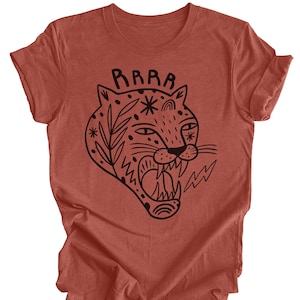 May include: A rust-colored t-shirt with a black graphic of a roaring tiger with a floral design and the word "RAAAAR" above it.