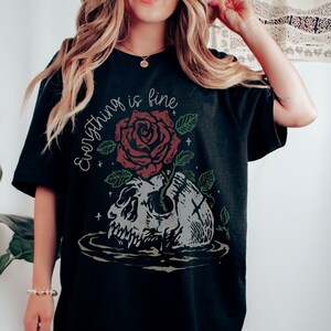 K&ouml;nnte beinhalten: Schwarzes Oversize-T-Shirt mit einem grafischen Druck eines Sch&auml;dels, aus dem eine Rose w&auml;chst. Der Text "Everything is fine" ist auf das Shirt gedruckt.