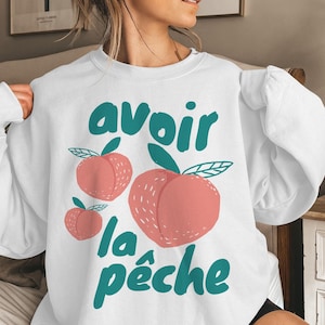 May include: White sweatshirt with a graphic design of peaches and the text "avoir la pêche" in teal.