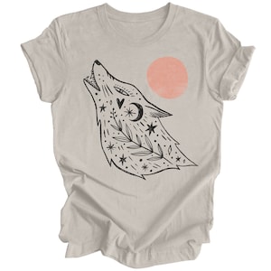May include: A heather grey t-shirt with a black and white illustration of a wolf howling at a pink sun. The wolf is surrounded by stars, leaves, and other celestial symbols.