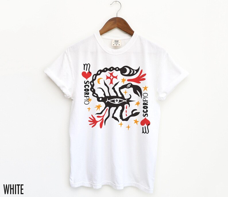 K&ouml;nnte beinhalten: Wei&szlig;es T-Shirt mit einem schwarzen Skorpion-Motiv und dem Wort "SCORPIO" in rot-schwarzer Schrift. Die Grafik enth&auml;lt auch rote Herzen, Sterne und andere Symbole.