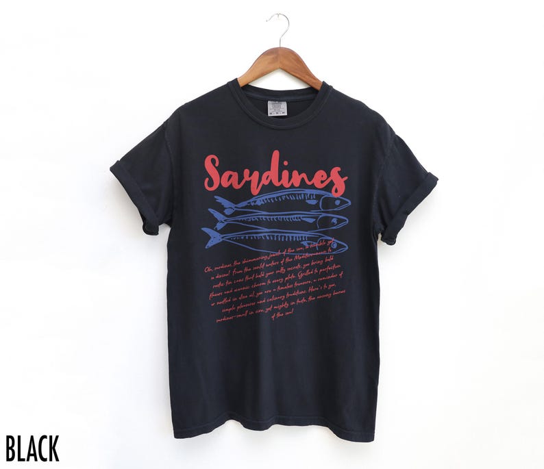 May include: Black t-shirt with a red and blue graphic of sardines and a text description about the fish. The text reads "Sardines" in red and the rest of the text is in blue.