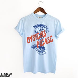 May include: A light blue t-shirt with a graphic of oysters and the text "Oysters Please" in red.