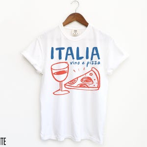K&ouml;nnte beinhalten: Wei&szlig;es T-Shirt mit einem blauen und roten Grafikdesign, auf dem "ITALIA vino e pizza" mit einem Glas Wein und einem St&uuml;ck Pizza steht.