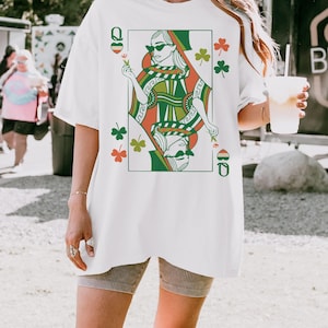 May include: White oversized t-shirt featuring a graphic print of a queen of hearts playing card with shamrocks. The queen is wearing sunglasses and holding a flower.