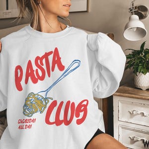 May include: White sweatshirt with a red and blue graphic that says "PASTA CLUB" with a drawing of a fork and noodles. The text "EVERYDAY ALL DAY" is also on the sweatshirt.