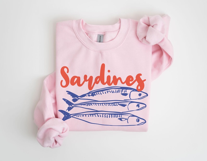 May include: Pink sweatshirt with the text "Sardines" in red and three blue sardines printed on the front.