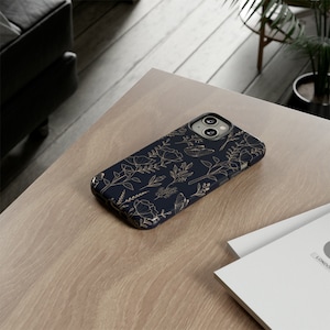 Puede incluir: Una funda para tel&eacute;fono azul marino con un patr&oacute;n floral dorado. La funda tiene un recorte para el objetivo de la c&aacute;mara.