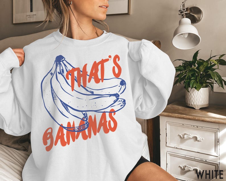 K&ouml;nnte beinhalten: Wei&szlig;er Pullover mit einem blauen und roten Aufdruck einer Bananenb&uuml;schel und dem Text "That's Bananas".