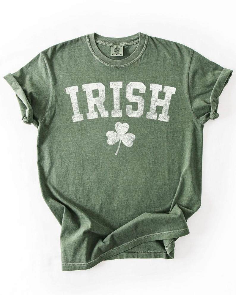 May include: Green t-shirt with the word "IRISH" in large, white, distressed letters and a white shamrock graphic. The shirt has rolled-up sleeves and a crew neck.
