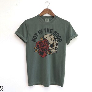 May include: A green t-shirt with a skull and rose graphic and the text "Not in the mood".