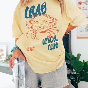 May include: A yellow t-shirt with a blue and red crab graphic and the text "Crab Lover Club" and "Everyday All Day".