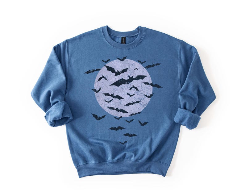 May include: A blue crew neck sweatshirt with a distressed graphic of a full moon and bats. The bats are black, and the moon is a lighter blue. The sweatshirt has rolled cuffs. The design is Halloween themed.