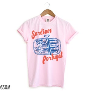 Op de afbeelding: Roze T-shirt met een afbeelding van een blikje sardines met de tekst "Sardines Portugal" erop gedrukt.