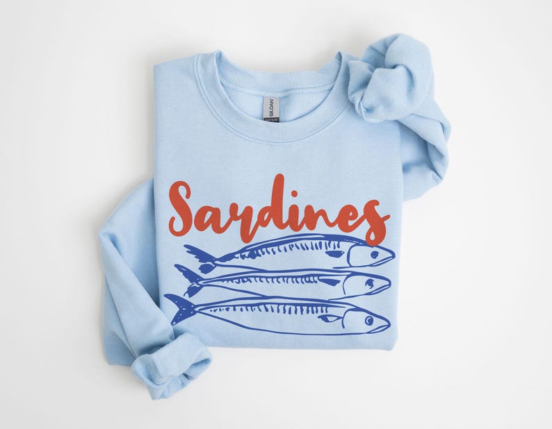 May include: A light blue sweatshirt with the word "Sardines" printed in red on the front. Three blue sardines are pictured below the word.