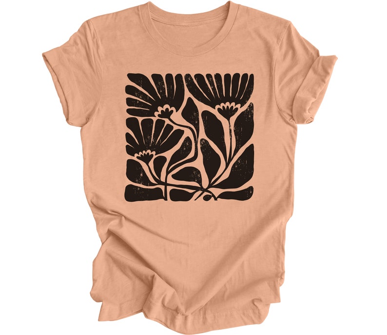 May include: A peach-colored t-shirt with a black floral print. The print is a stylized design of flowers and leaves.