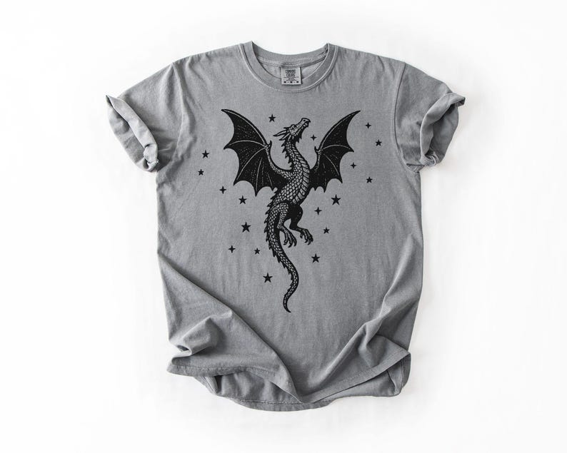 Op de afbeelding: Grijs T-shirt met een zwart drakenontwerp. De draak heeft uitgespreide vleugels en is omringd door kleine zwarte sterren. Het shirt heeft een ronde hals en korte mouwen.