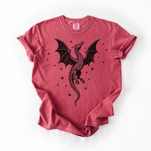 Op de afbeelding: Rood T-shirt met een zwart drakenontwerp. De draak heeft grote vleugels en is omringd door sterren. De mouwen zijn opgerold. Het T-shirt heeft een ronde hals.