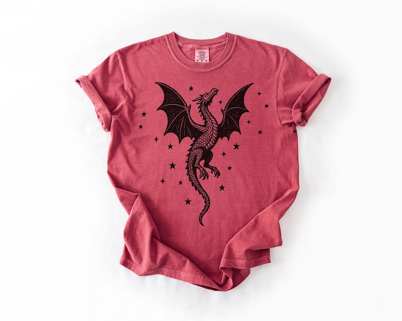 Op de afbeelding: Rood T-shirt met een zwart drakenontwerp. De draak heeft grote vleugels en is omringd door sterren. De mouwen zijn opgerold. Het T-shirt heeft een ronde hals.