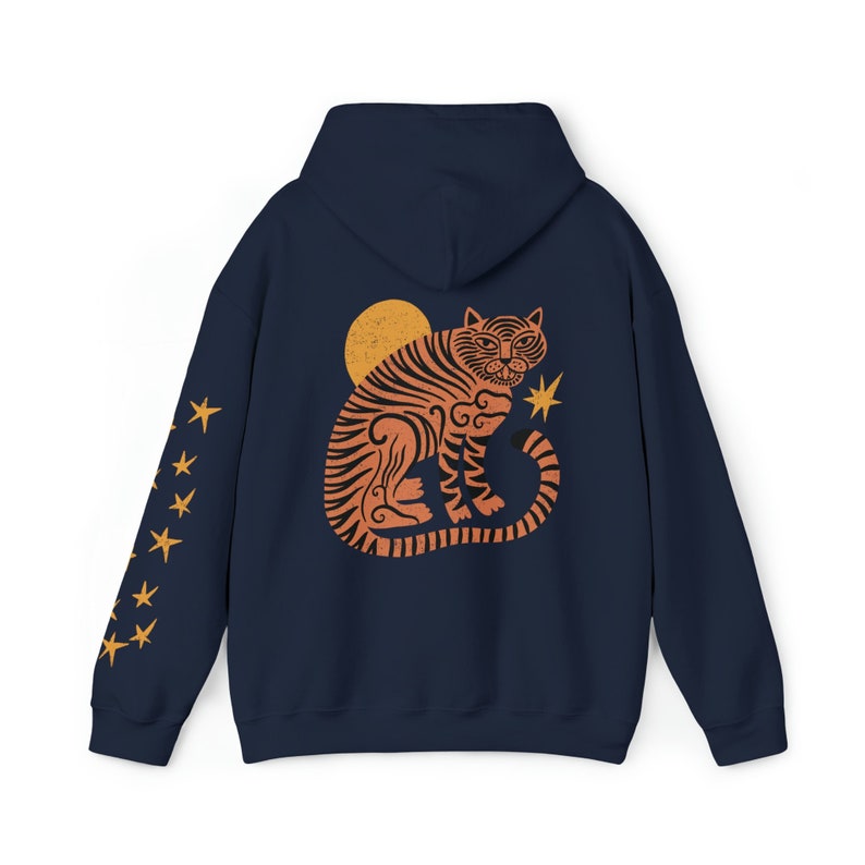 May include: A navy blue hoodie with a stylized orange tiger design on the back. The tiger is sitting with its tail curled around its body. There is a yellow sun and a yellow star behind the tiger. The sleeves of the hoodie have yellow stars printed on them.