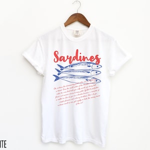 May include: White t-shirt with a red and blue graphic of sardines and text that reads "Sardines" and "Oh, sardines, the shimmering jewels of the sea... you are a treasure from the wild waters of the Atlantic..."