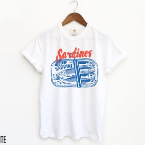 K&ouml;nnte beinhalten: Wei&szlig;es T-Shirt mit einer blauen und roten Grafik einer Sardinenb&uuml;chse. Der Text auf der Dose lautet "Sardine" und "Sardines".