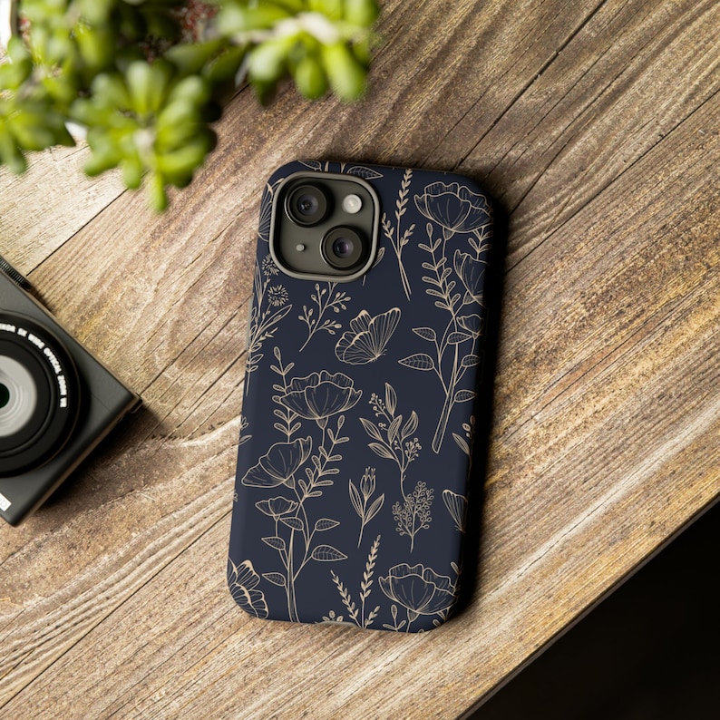 Puede incluir: Una funda para tel&eacute;fono azul marino con un patr&oacute;n floral dorado. La funda tiene un recorte para la lente de la c&aacute;mara.