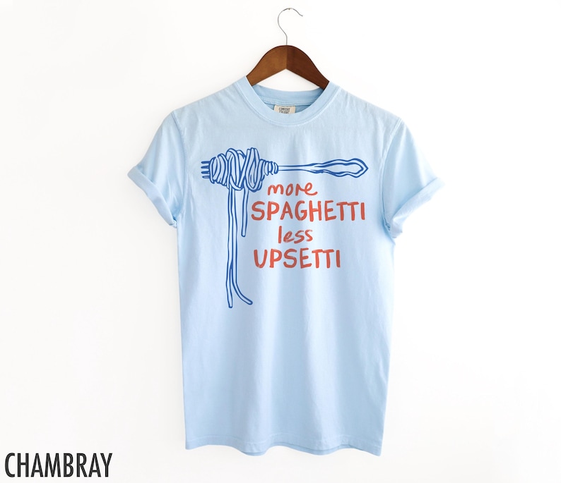 May include: Light blue t-shirt with a blue and white illustration of spaghetti and the text "more spaghetti less upsetti" in red and blue.