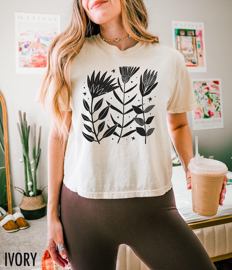 May include: Ivory t-shirt with a black floral design, leaves, and stars. The shirt has a relaxed fit and short sleeves. The word "IVORY" is printed at the bottom left of the image.