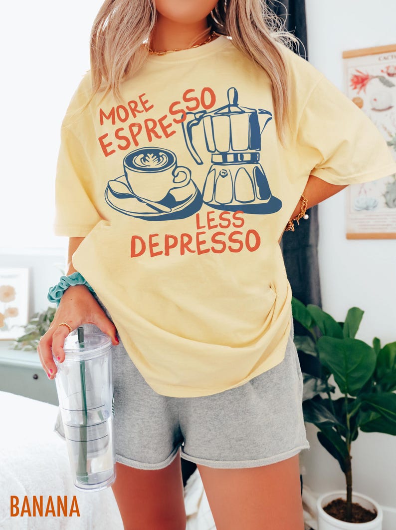 May include: A yellow t-shirt with the text "More Espresso Less Depresso" in red and blue lettering. The design features a coffee cup and a coffee pot.