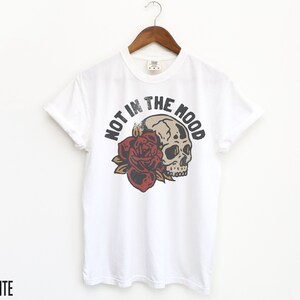 May include: White t-shirt with a skull and rose graphic and the text "Not in the Mood".