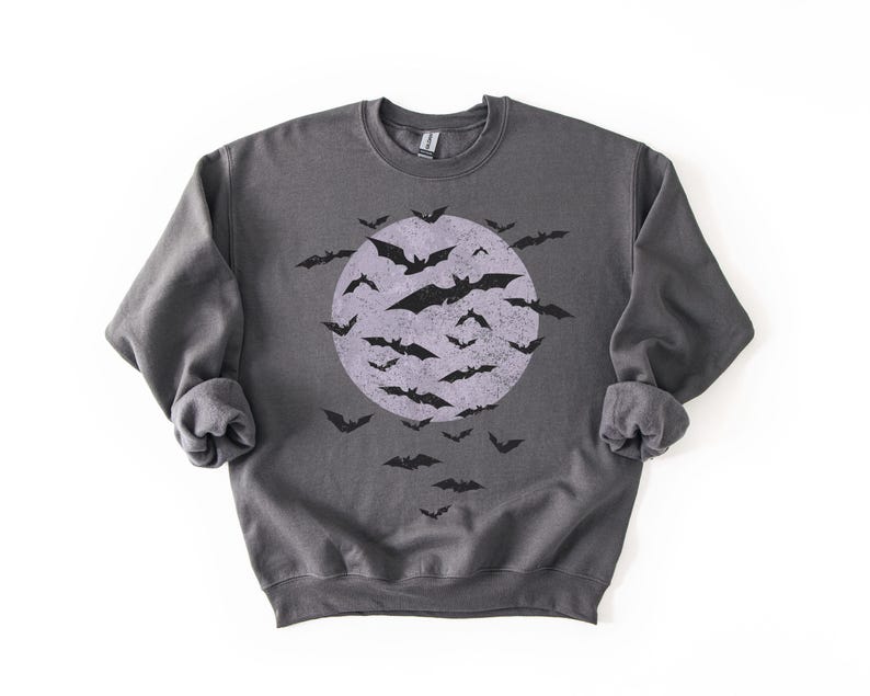 May include: A dark grey sweatshirt with a distressed graphic of a full moon and bats. The bats are black, and the moon is a faded purple. The sweatshirt has long sleeves and a crew neck, perfect for Halloween.