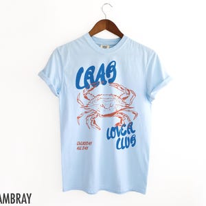 May include: Light blue t-shirt with a blue and red crab graphic and the text "Crab Lover Club" and "Everyday All Day".