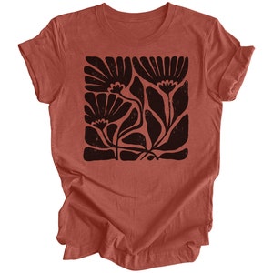 May include: A rust-colored t-shirt with a black floral print. The print is a stylized design of flowers and leaves.