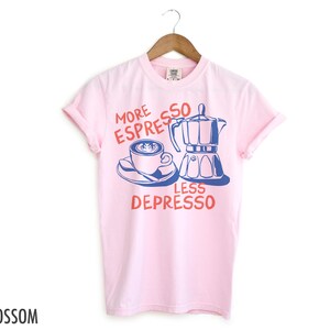 May include: Pink t-shirt with a blue and white illustration of a coffee pot and a cup of coffee. The text on the shirt reads "More Espresso Less Depresso".