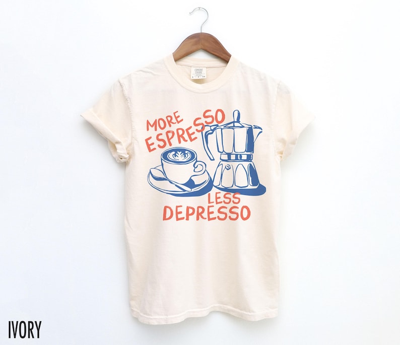 May include: A cream colored t-shirt with a blue and red graphic of a coffee pot and a cup of coffee. The text on the shirt reads "More Espresso Less Depresso".