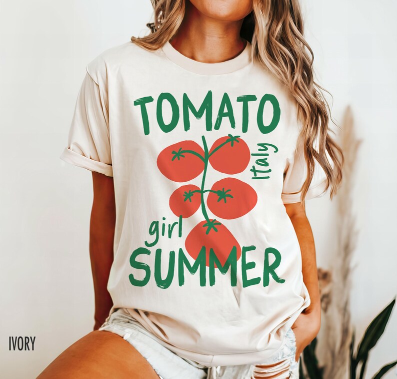 May include: A cream-colored t-shirt with a graphic of a tomato plant with the text "Tomato girl summer Italy" printed on it.
