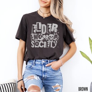 May include: A dark brown t-shirt with a white graphic print that says "FLDER EMO SOCIETY" with skull and crossbones.