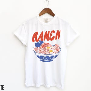 May include: White t-shirt featuring a red graphic of a bowl of ramen noodles. The text "RAMEN" is printed in red above the bowl.