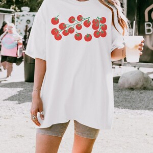 May include: White oversized t-shirt with a graphic of red tomatoes on a vine. The shirt is made of a soft, comfortable material.