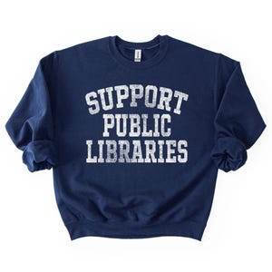 May include: Navy blue sweatshirt with the text "SUPPORT PUBLIC LIBRARIES" in distressed white lettering. The crew neck sweatshirt is a casual style, perfect for showing support for libraries.