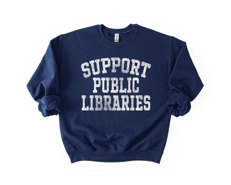 May include: Navy blue sweatshirt with the text "SUPPORT PUBLIC LIBRARIES" in distressed white lettering. The crew neck sweatshirt is a casual style, perfect for showing support for libraries.