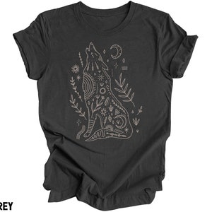 May include: A dark heather grey t-shirt with a graphic of a howling wolf with intricate geometric patterns and floral elements. The wolf is surrounded by stars, moons, and other celestial symbols.