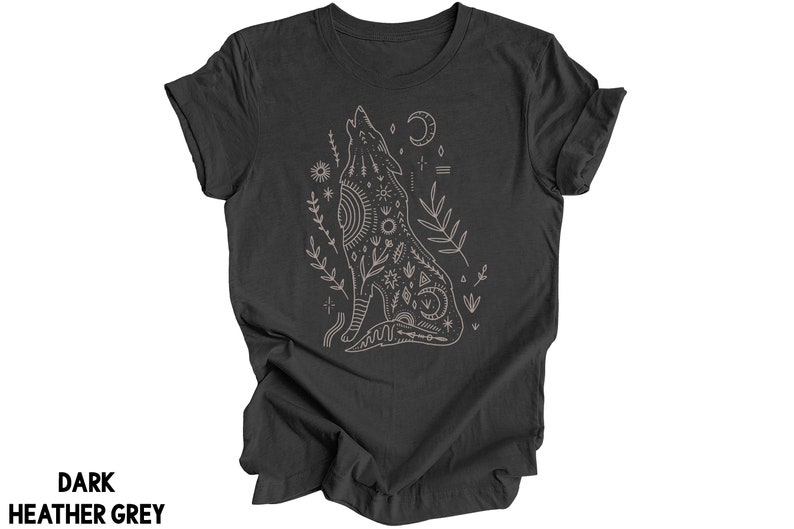 May include: A dark heather grey t-shirt with a graphic of a howling wolf with intricate geometric patterns and floral elements. The wolf is surrounded by stars, moons, and other celestial symbols.