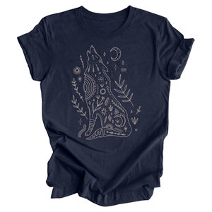 May include: A navy blue t-shirt with a white outline of a howling wolf with intricate geometric patterns and floral accents. The wolf is surrounded by stars, moons, and other celestial symbols.