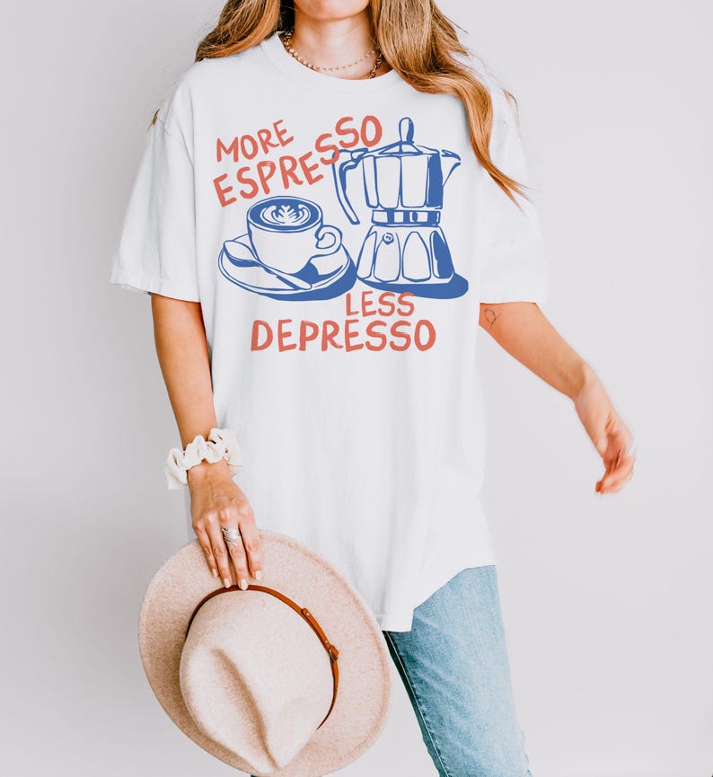 K&ouml;nnte beinhalten: Wei&szlig;es T-Shirt mit einem Kaffee-Motiv. Das Design zeigt eine Kaffeetasse, einen Espressokocher und den Text "MORE ESPRESSO LESS DEPRESSO" in Rot und Blau. Das Shirt wird mit einer blauen Jeans und einem beigen Hut getragen.