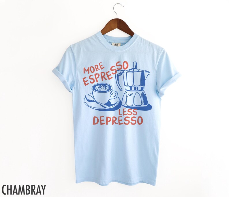 May include: Light blue t-shirt with a graphic of a coffee cup and a coffee pot. The text on the shirt reads "More Espresso Less Depresso".